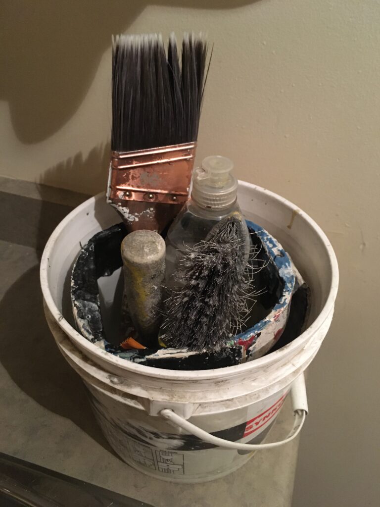 A small cleaning bucket with a paint brush and brush cleaning equipment. This is part of the basic tool set for painting a house.