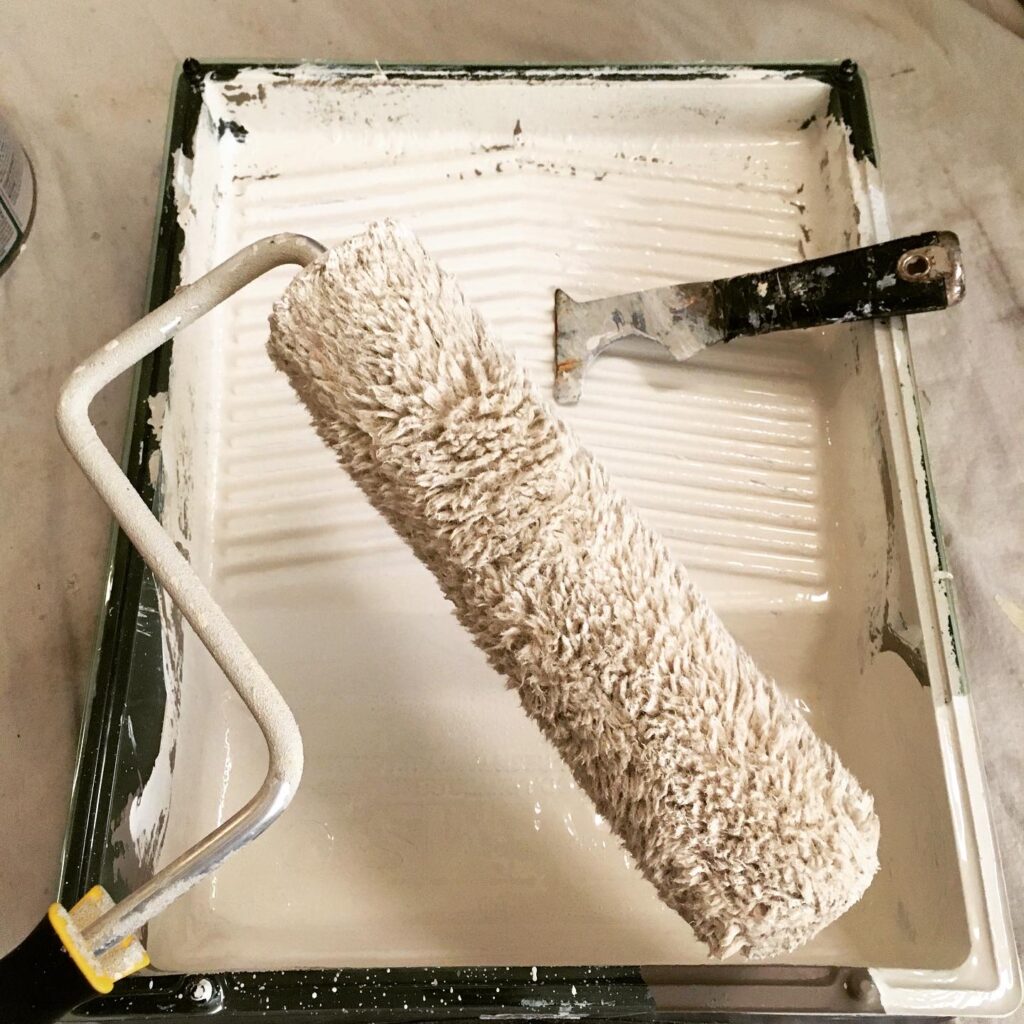 This paint roller has been scraped dry with a 5-in-1 painters tool. The paint has been poured out of the roller tray and then the dry roller was used to soak up the residual paint in the roller tray.